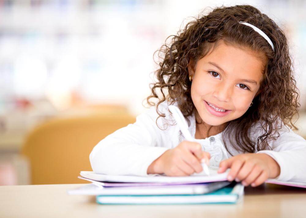 Cute,Little,Girl,Studying,At,The,Library,And,Smiling - Summit K12 the benefits of being a multilingual speaker