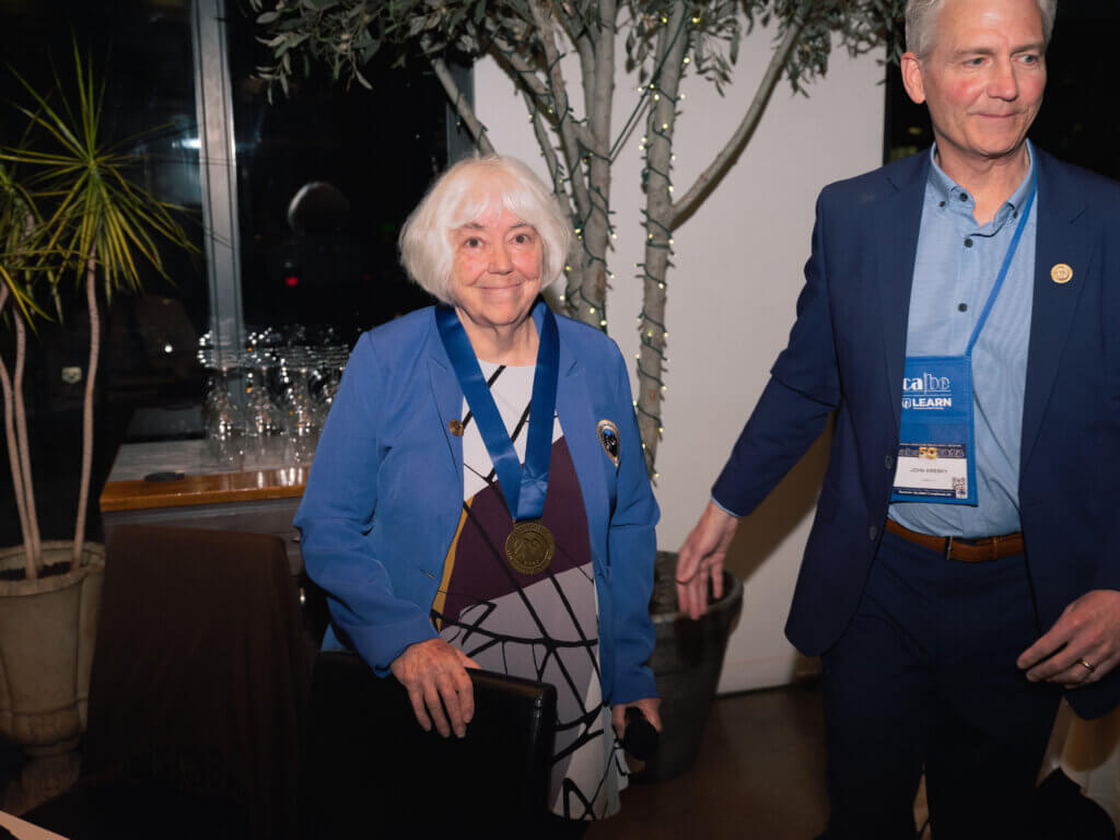 Dr. Alma Flor Ada pictured wearing her blue Multilingual Education Hall of Fame coat and medal next to Summit K12's President and CEO, John Kresky.